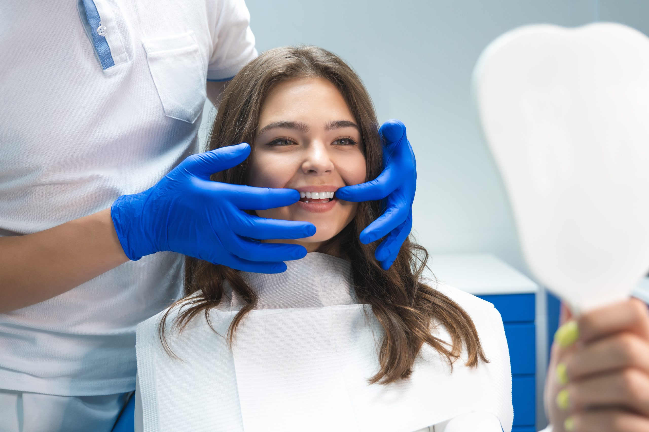 beautiful young brunette woman having examination at dentist office while dentist showing whitening results to patient.