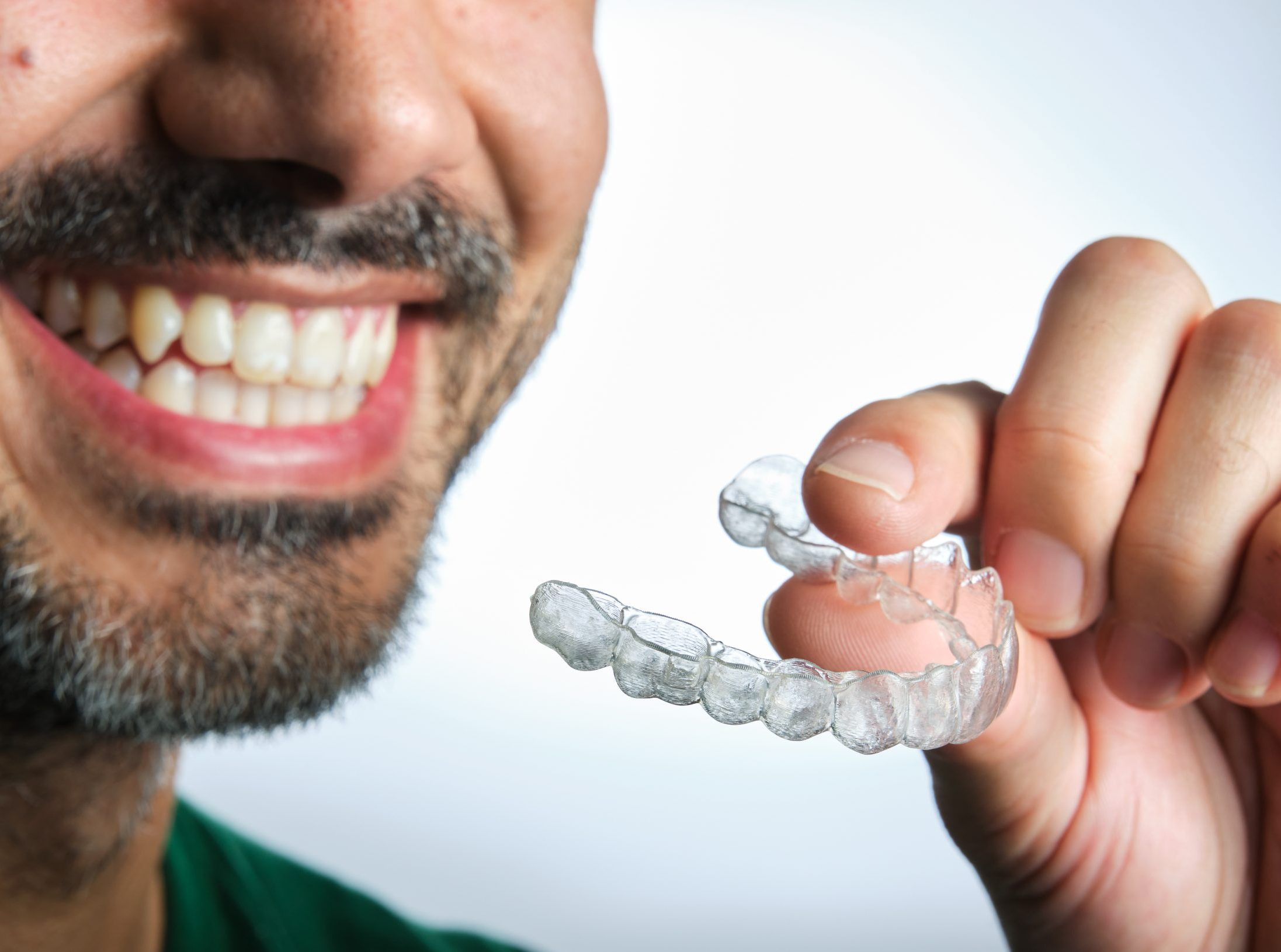 unrecognizable dark-haired man with beard putting on transparent dental retainer