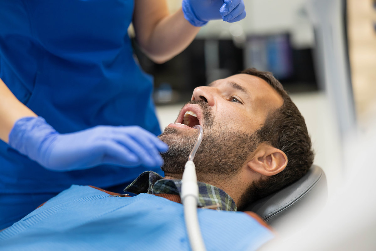 A patient is seated in a dentist's chair with a focus on care and hygiene, receiving careful attention from a dental professional in a modern clinic during a procedure.