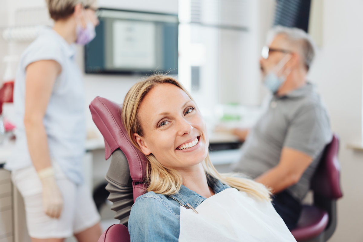 Happy young woman in a dental surgery waiting on the examination couch as the dentist and nurse have a discussion behind