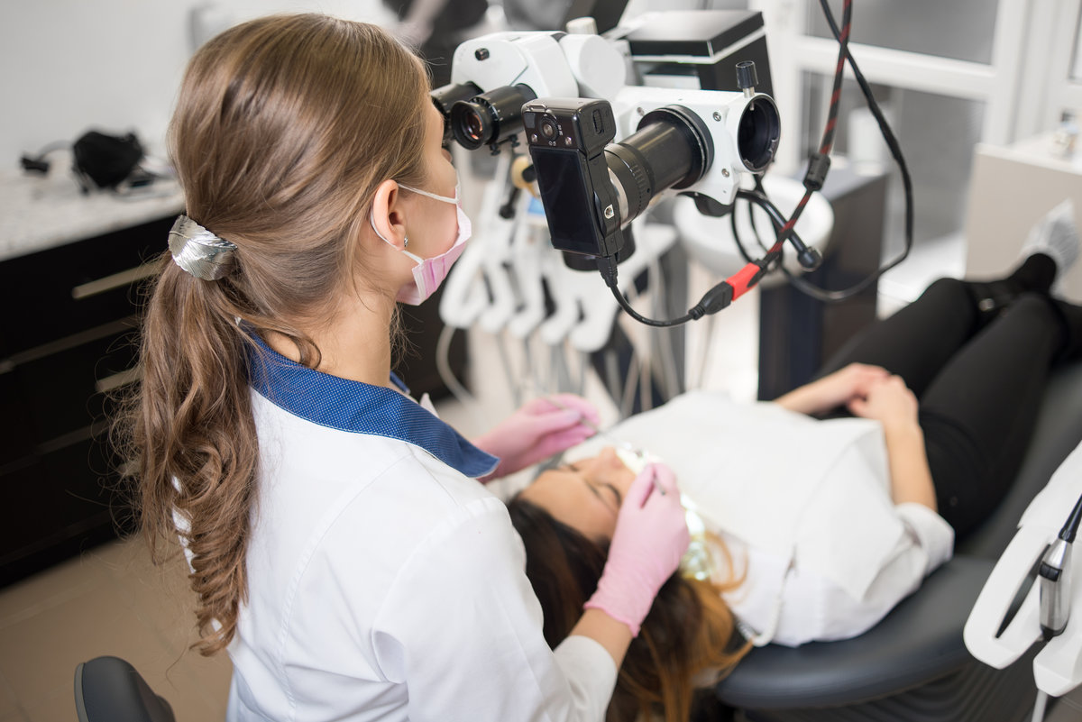 Female dentist with dental tools - microscope, mirror and probe checking up patient teeth at dental clinic office. Medicine, dentistry and health care concept. Dental equipment
