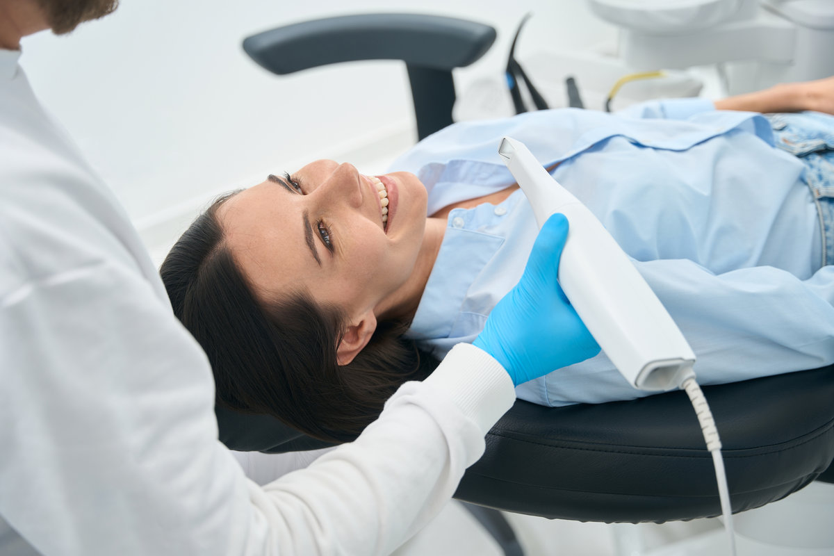 Smiling woman lying in orthodontic chair, preparing for doctor checking her mouth health with dental intraoral camera, private clinic service