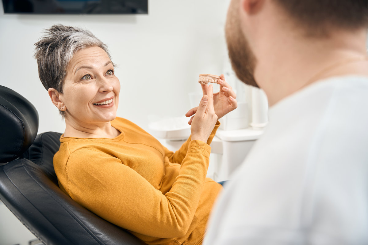 Surprised woman holding in hands 3d model of her upper teeth, consulting with aesthetic dentist about tooth align and straighten, positioning of them with regard to her bite with dental braces