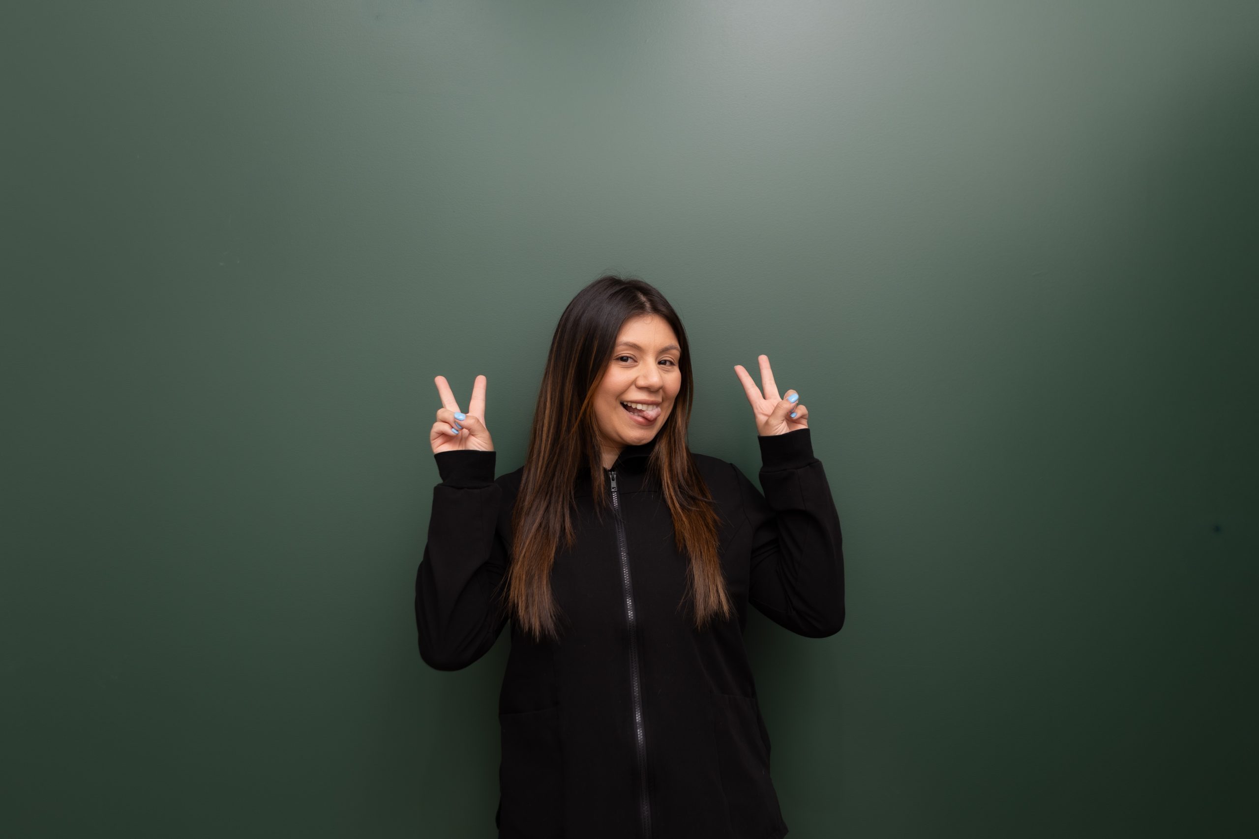 Woman in black jacket making peace signs with both hands against green background