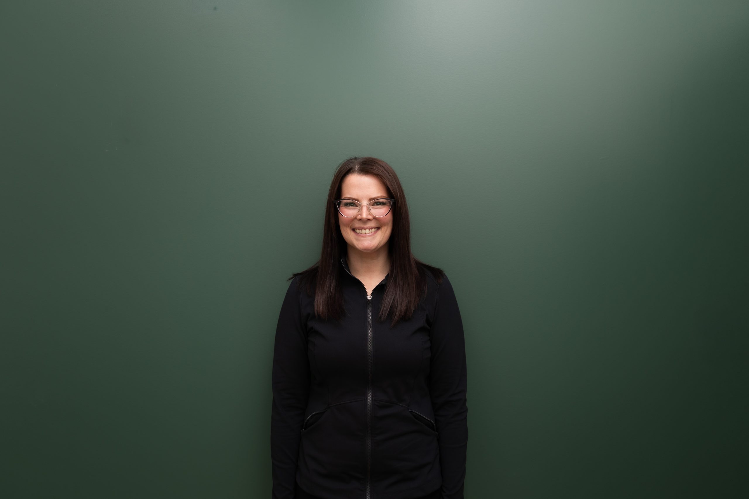 Woman in black jacket smiling at camera against green background, professional headshot