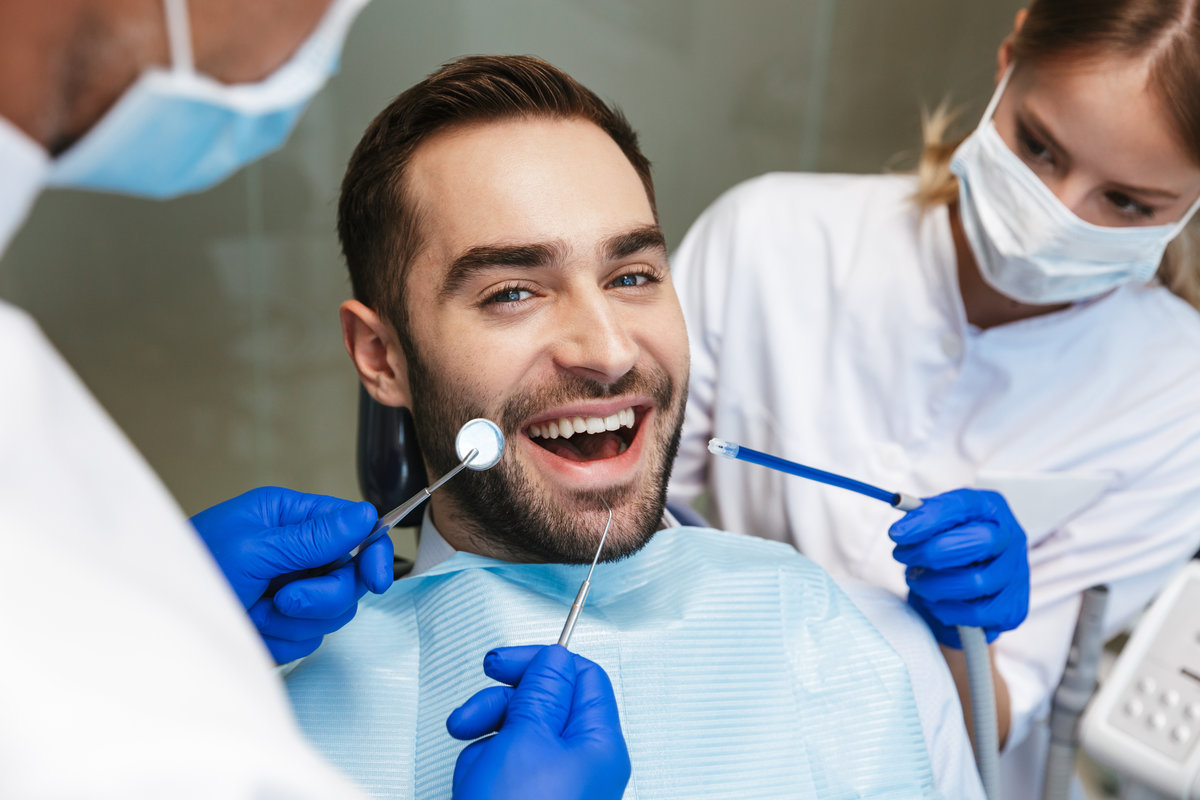 Image of a handsome happy young man sitting in medical dentist center. Looking at camera.
