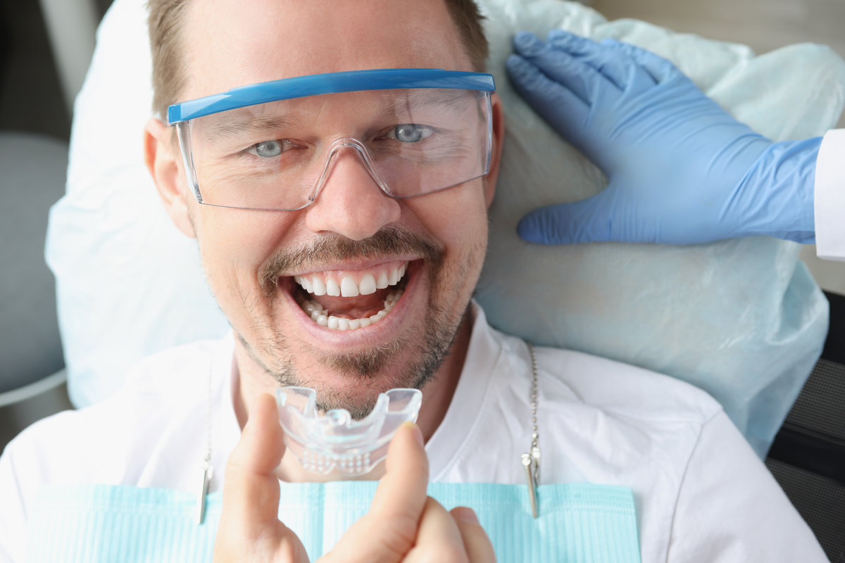 Dentist doctor inserting plastic night guard to man in dental office. Professional teeth whitening concept