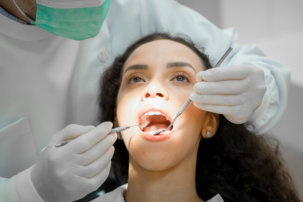 Dentist holding a tooth mirror and dental pick are performing dental exam on a patient in dental clinic