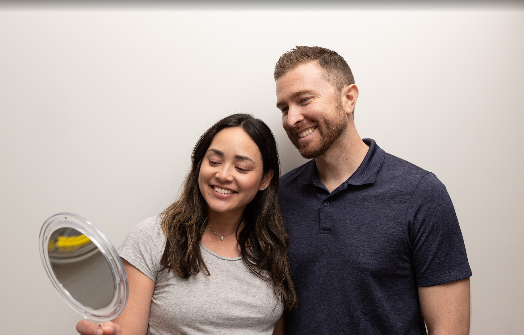 Couple looking at their smiles in a handheld mirror after cosmetic dental treatment at Evergreen Grace Dental Care in Renton, WA